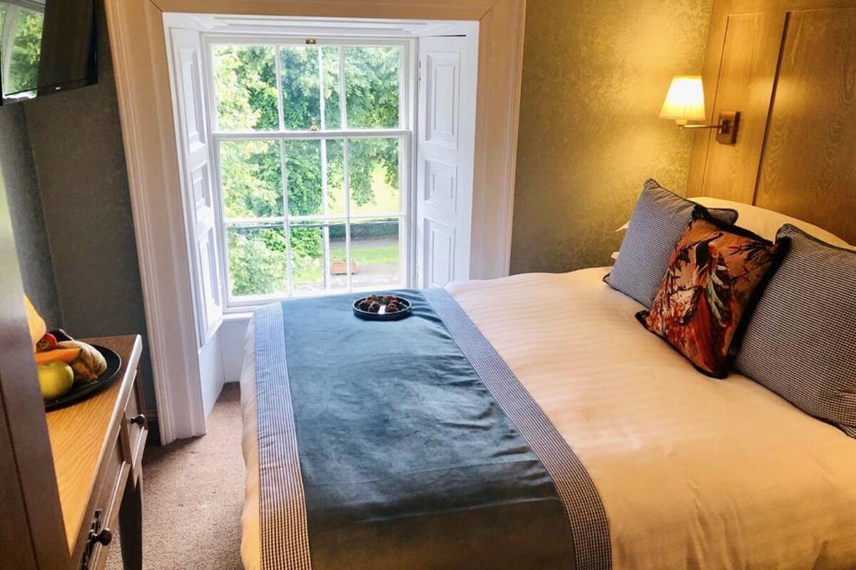 Un dormitorio con cama, ventana, lámpara y una mesita con frutas.
