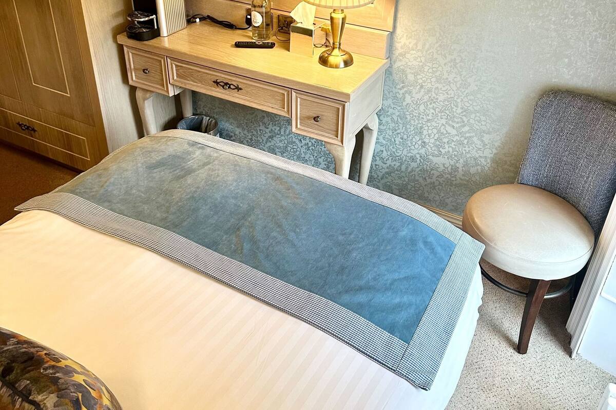 Habitación de hotel con cama, escritorio con lámpara, silla y televisor montado en la pared.