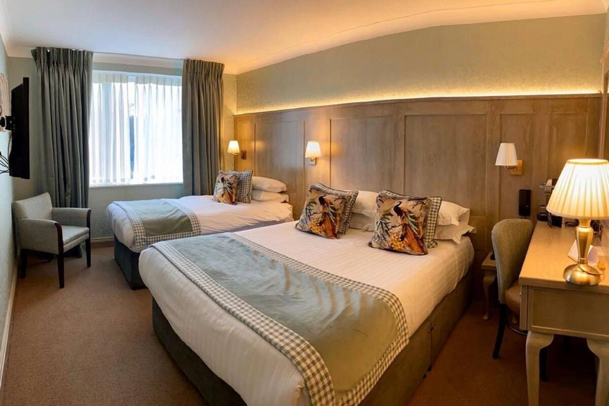 Habitación de hotel con dos camas, un escritorio, una silla y un televisor.