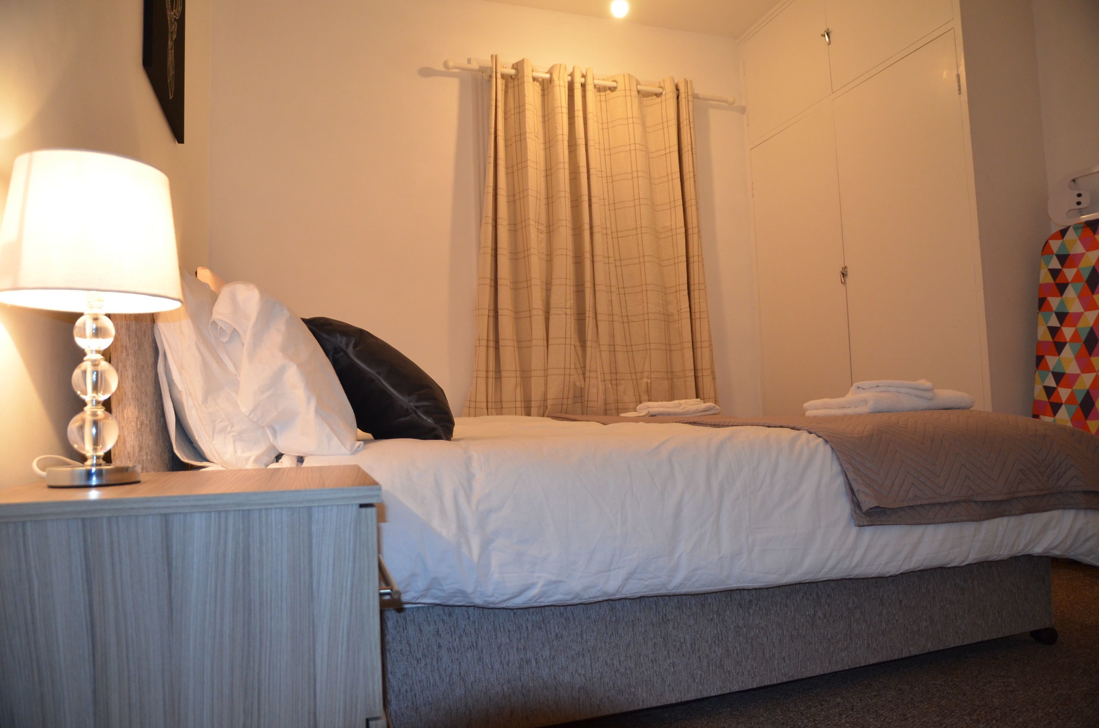 A neatly made bed with white linens, a bedside lamp, and a folded towel on the nightstand.