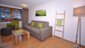 A modern living room with a grey sofa, green cushions, a wooden coffee table, a ladder, and a painting on the wall. - Berghüs Schratt - vegetarisches und veganes Biohotel (Oberstaufen)