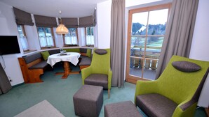 A cozy room with a dining table, two green armchairs, a bench, and a view of a snowy landscape through a large window. - Berghüs Schratt - vegetarisches und veganes Biohotel (Oberstaufen)