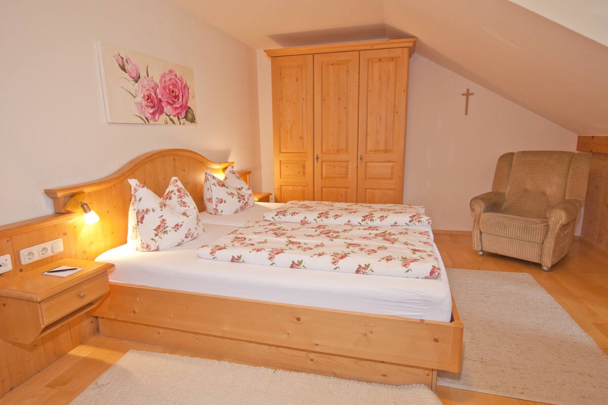 Quarto com cama de madeira, mesas de cabeceira, uma cadeira e um guarda-roupa.
