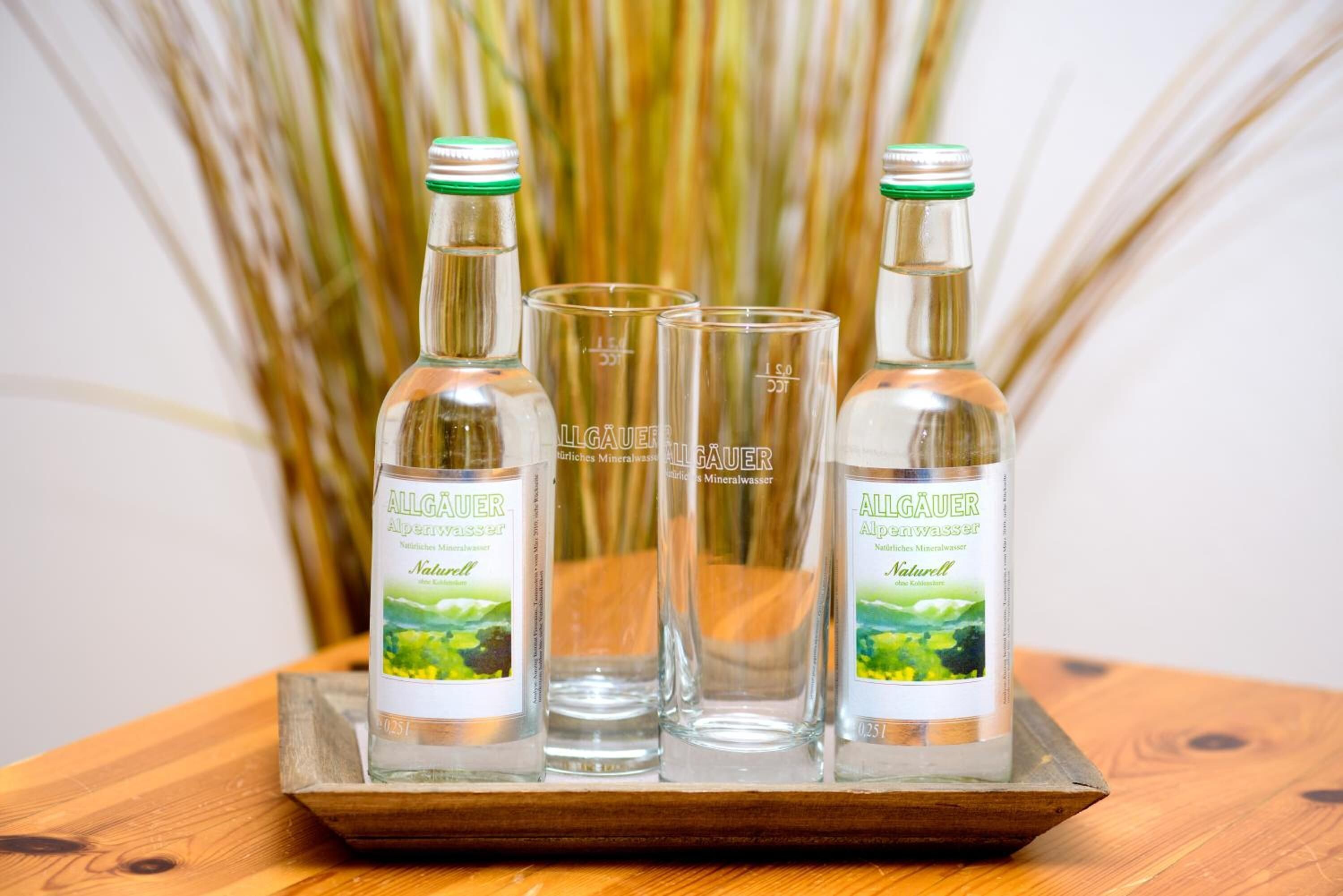Drie flessen en twee glazen Allgäuer mineraalwater op een houten dienblad.