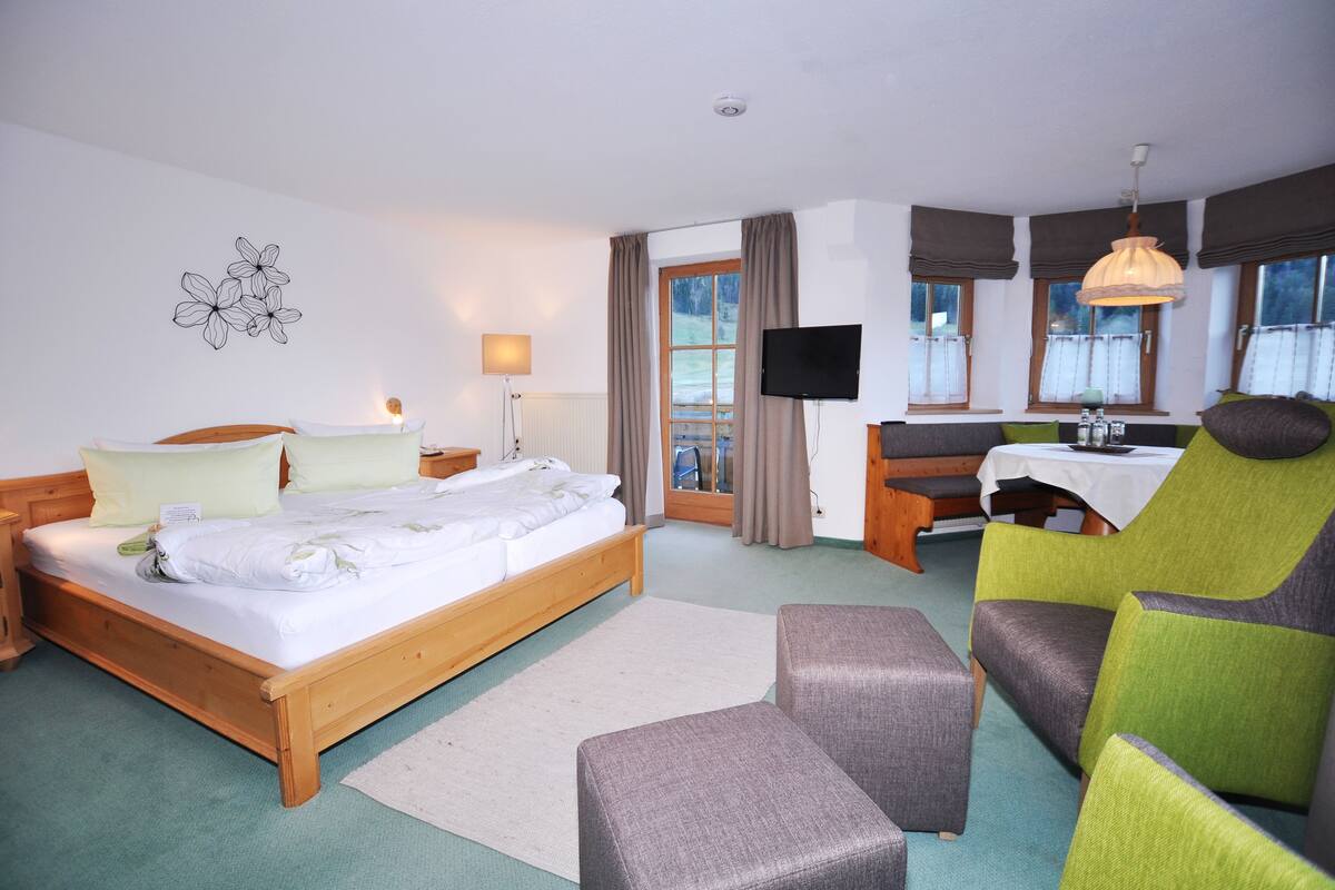 Quarto de hotel com cama de madeira, escrivaninha, televisão e vista para o exterior.