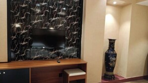 Una habitación con un televisor fijado a una pared de mármol, un mueble de madera, un banco y un jarrón decorativo.
