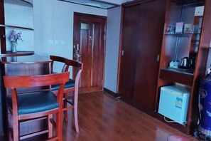 A room with a wooden dining table and chairs, a small refrigerator, and a cabinet with shelves. - Huaxia Hotel (Yingkou)