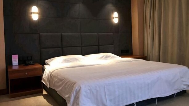 Habitación de hotel con una cama grande, cabecera con iluminación integrada, mesita de noche y cortina.