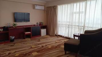 Habitación de hotel con un ventanal grande, un televisor de pantalla plana en la pared, un escritorio pequeño con una silla y un sofá.