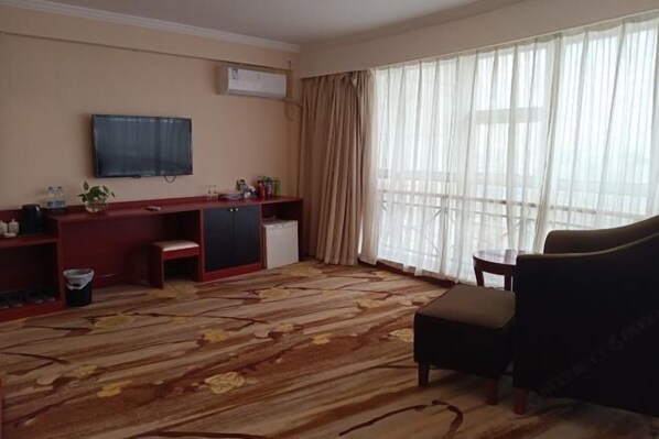 Habitación de hotel con un ventanal grande, un televisor de pantalla plana en la pared, un escritorio pequeño con una silla y un sofá.