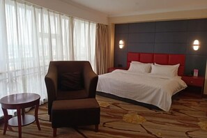 A hotel room with a bed, a chair, a small table, and a large window with curtains. - Huaxia Hotel (Yingkou)