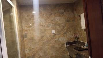 Un baño con paredes de mármol, un inodoro, un lavamanos con espejo y un florero con flores.