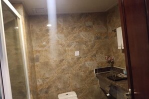 A bathroom with marble walls, a toilet, a sink with a mirror, and a vase with flowers. - Huaxia Hotel (Yingkou)