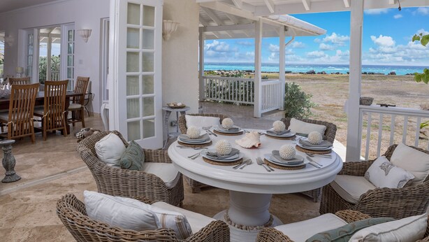 A covered outdoor dining area with wicker furniture and a view of the ocean. - Whispering Palms (Belair)