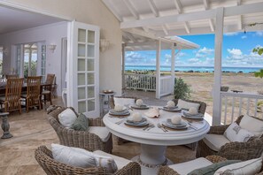A covered outdoor dining area with wicker furniture and a view of the ocean. - Whispering Palms (Belair)