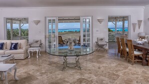 A spacious living room with a glass table, a beige sofa, and a view of the ocean through large windows. - Whispering Palms (Belair)