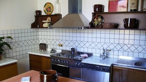 Una cocina con estufa, horno y pileta. Hay una mesa con un mantel individual y un libro.