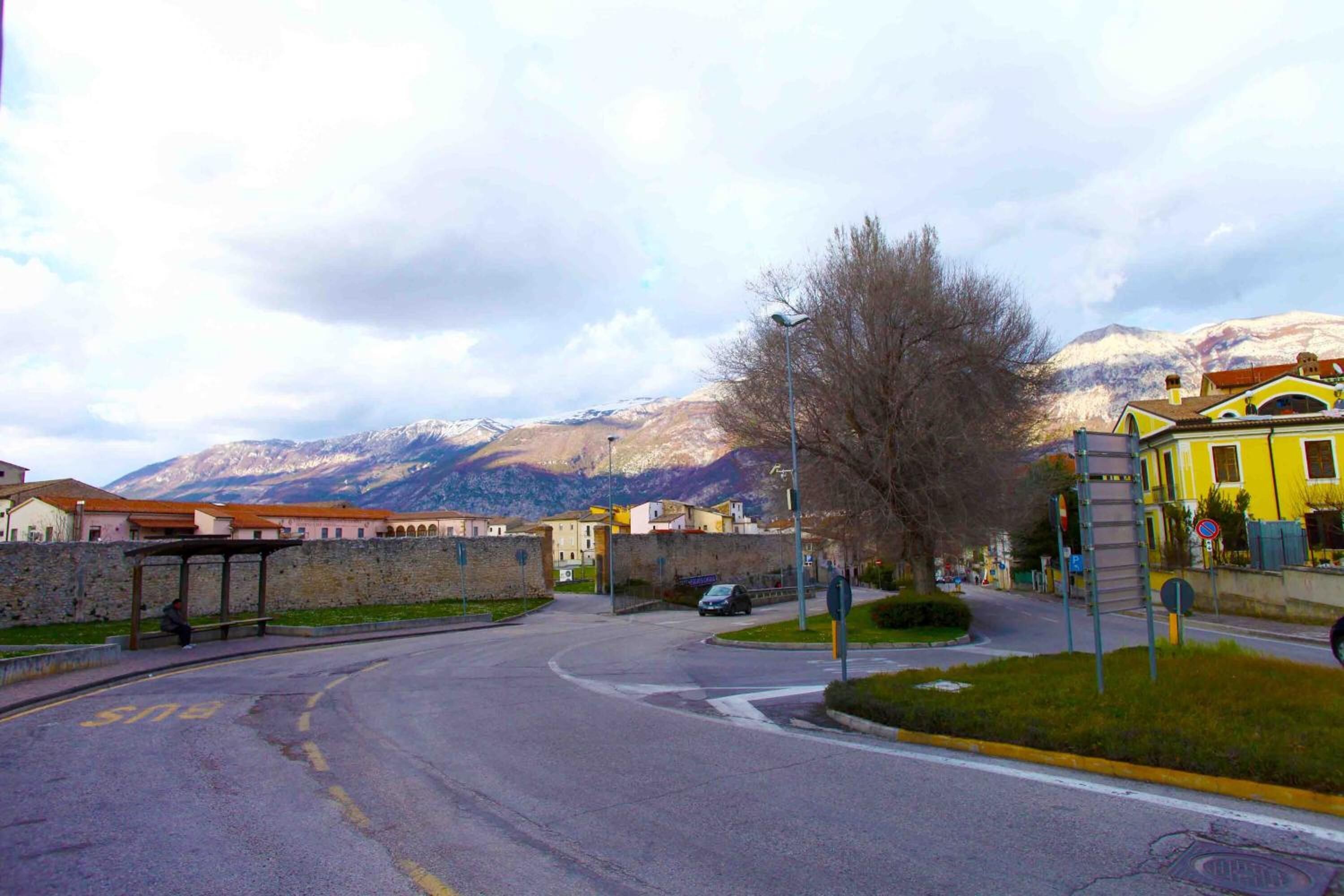 A street with a bus stop, a yellow building, and mountains in the background.