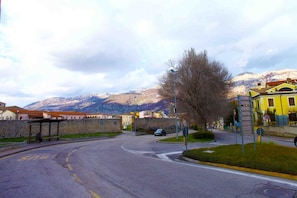 A street with a bus stop, a yellow building, and mountains in the background. - B&B Santa Chiara (Sulmona)