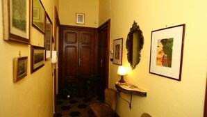 Un pasillo estrecho con una puerta de madera, una lámpara de pared y varias fotografías enmarcadas.