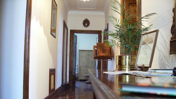 Un pasillo con suelo de madera, un mostrador de recepción, una planta en maceta y certificados enmarcados.