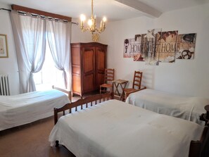 A room with two single beds, a wooden wardrobe, a small table with chairs, and a chandelier.