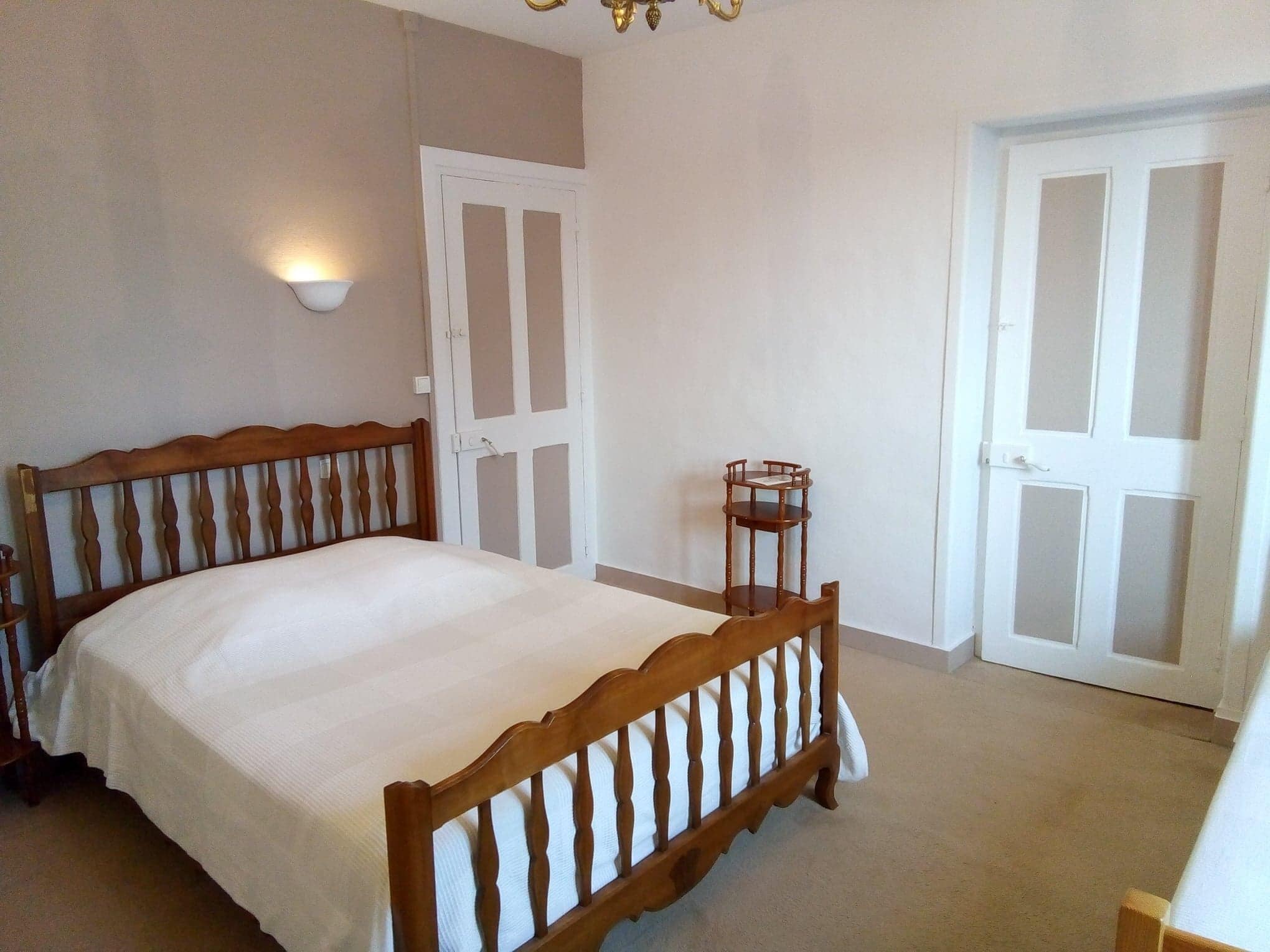 Un dormitorio con cama de madera, paredes blancas, una mesita y dos puertas.