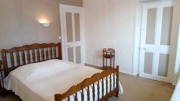 Un dormitorio con cama de madera, paredes blancas, una mesita y dos puertas.