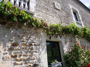 A stone building with a window and a door, vines growing along the wall, and a potted plant near the entrance. - La Mare Aux 3 Diables Chambre d'Hôtes (Fresney-le-Vieux)