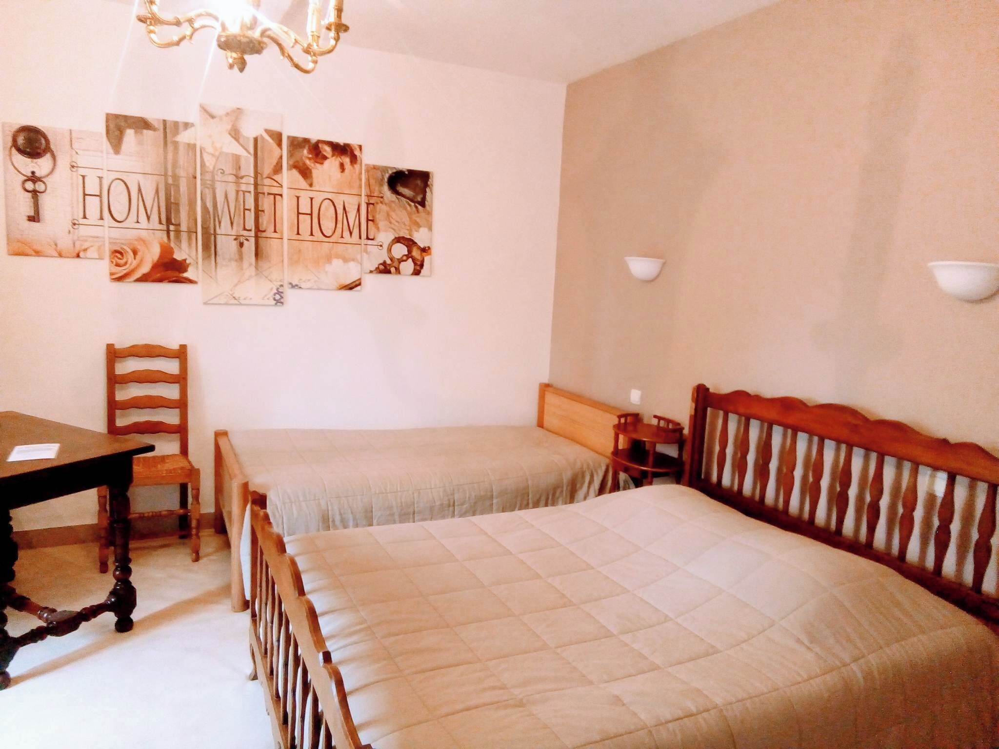 A bedroom with two beds, a wooden chair, a table, and wall art.