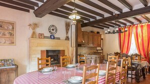 Un coin repas avec une nappe à carreaux, des chaises en bois, une cheminée et une cuisine en arrière-plan.
