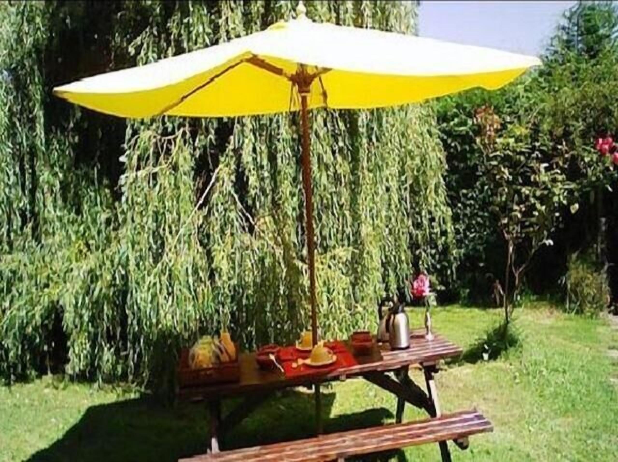 A picnic setup with a yellow umbrella, a wooden table, and a metal pot.