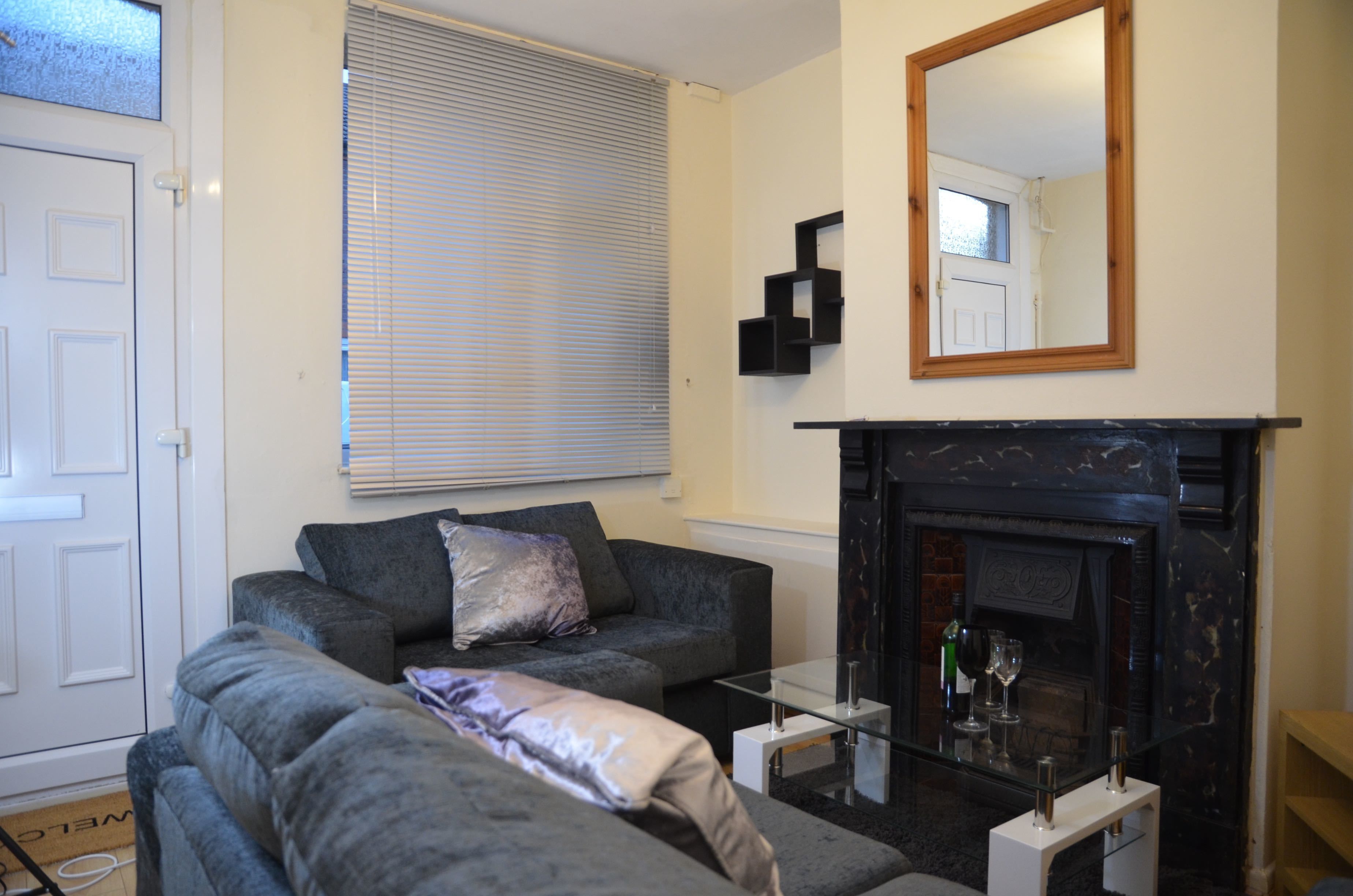 A living room with a fireplace, a sofa, a glass coffee table, and a mirror on the wall.