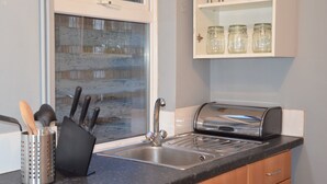 A kitchen with a stainless steel sink, a toaster, and a knife block. There are jars on a shelf above the sink. - People Boxes Apartments - 38 Ridgway (Luton)