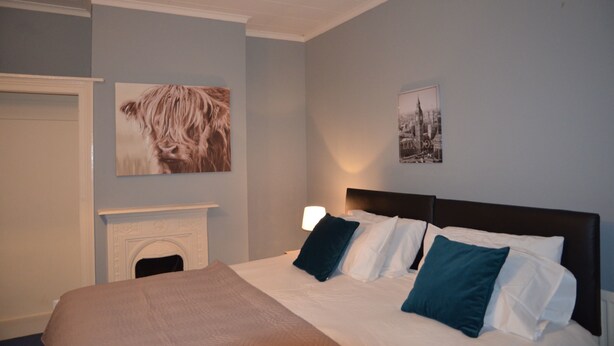 A bedroom with a bed, a fireplace, and two framed pictures on the wall. - People Boxes Apartments - 38 Ridgway (Luton)