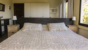 A large bed with a patterned bedspread, two bedside tables with lamps, a wardrobe, and a window with curtains.