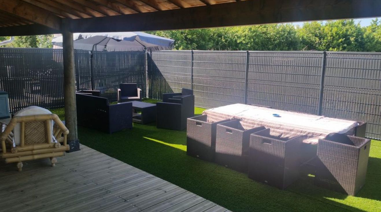 An outdoor patio with artificial grass, a wooden deck, and a covered seating area with a table and chairs.