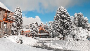 Ein schneebedecktes Gebäude mit Steinmauern und hölzernen Balkonen, umgeben von mit Schnee beladenen Bäumen.