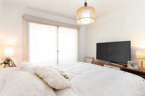 Hotellihuone, jossa on suuri sänky, taulutelevisio, yöpöytä lampun kanssa ja ikkuna, jossa on sälekaihtimet.