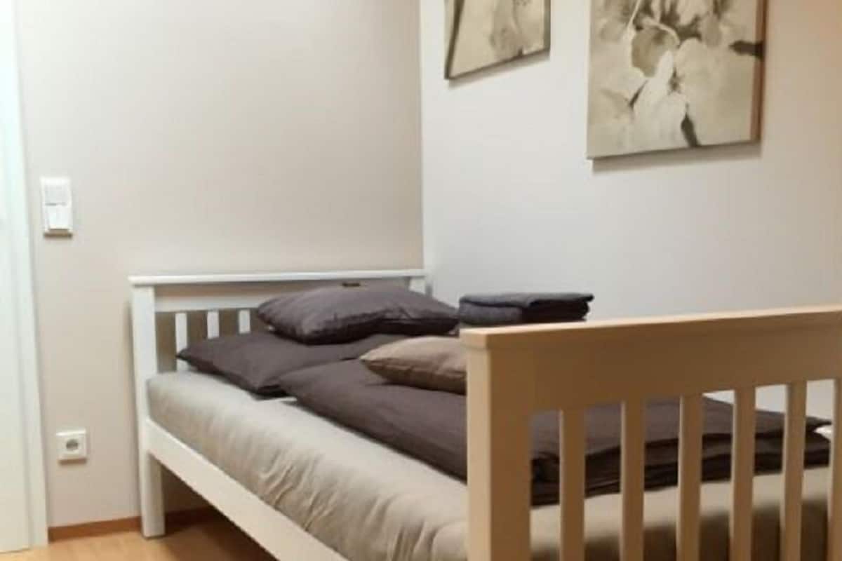Een enkel bed met een houten hoofdbord, grijze beddengoed en twee abstracte kunstwerken aan de muur.