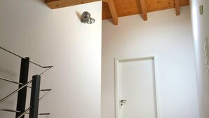 A room with a wooden ceiling, a white door, and a black staircase.