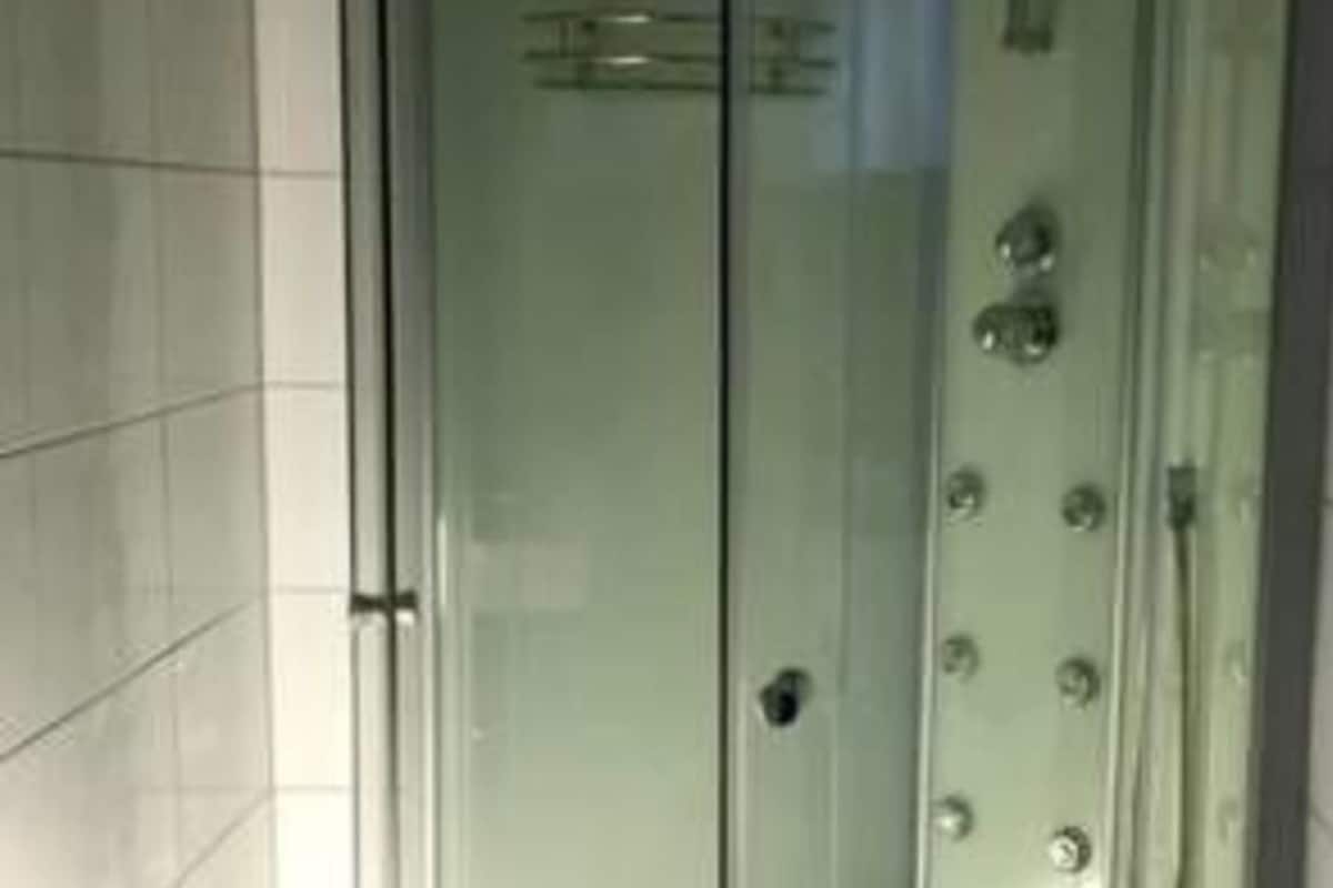 Een douchecabine met glazen wanden, een gebogen ontwerp, een zichtbare douchekop en een betegelde vloer.