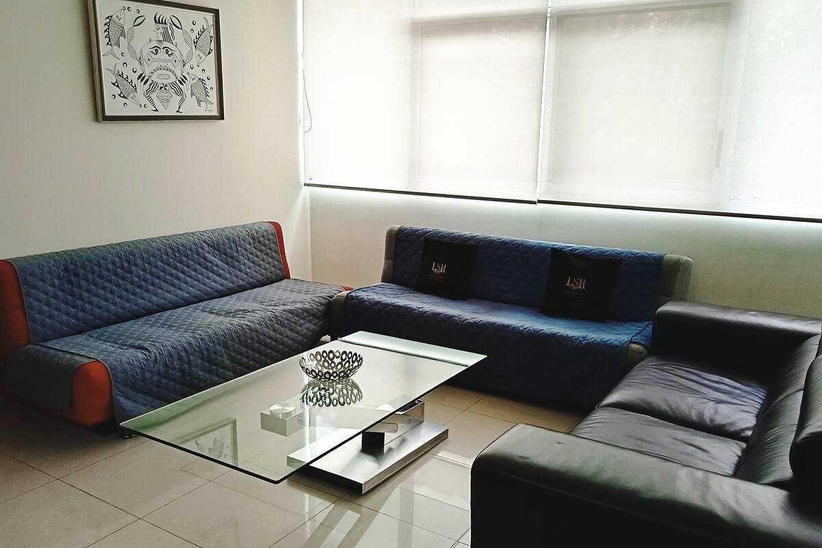 Una sala de estar moderna con un sofá azul, un sofá de cuero negro y una mesa de centro de vidrio.