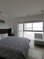 Une chambre d’hôtel avec un grand lit, une table de chevet, une chaise et une vue sur la mer.