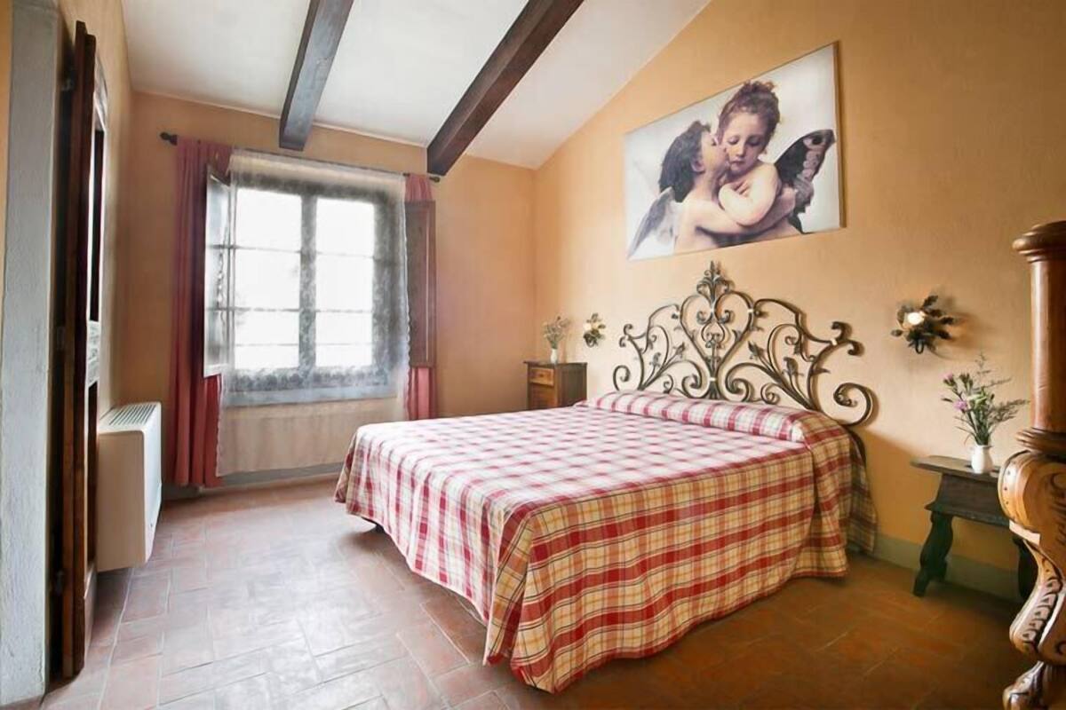 Une chambre à coucher avec un lit, une fenêtre avec des rideaux, un tableau au mur et une table de chevet avec un vase.