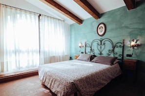 Een slaapkamer met een bed, gordijnen, een wandlamp en een ingelijste foto.