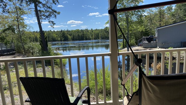 Un muelle de madera con una silla y una hamaca con vista a un lago.