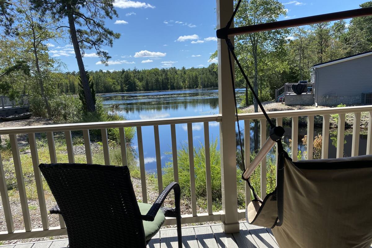 A wooden deck with a chair and a hammock overlooking a lake.