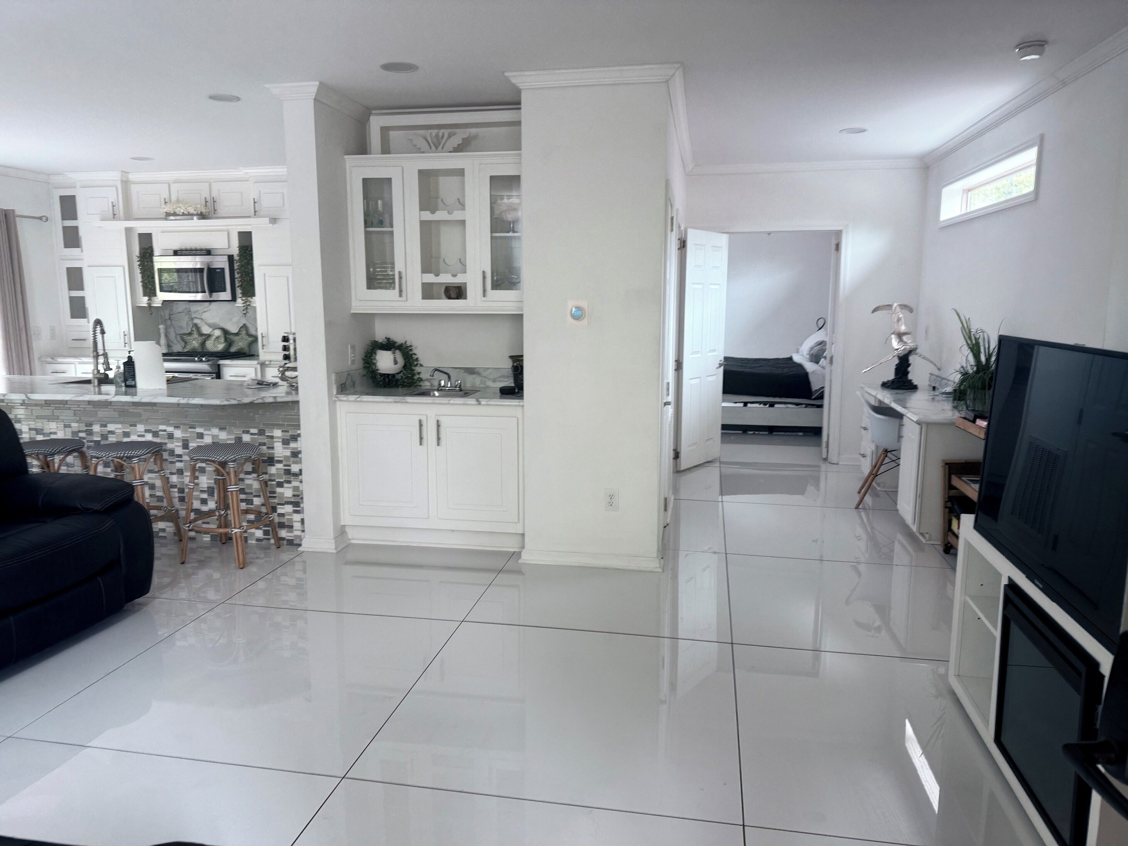A modern kitchen with white cabinets, a central island, and a dining area with a black sofa and stools.
