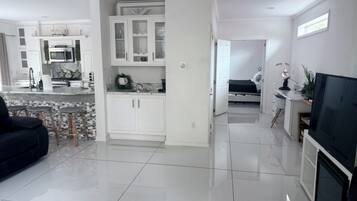 A modern kitchen with white cabinets, a central island, and a dining area with a black sofa and stools.